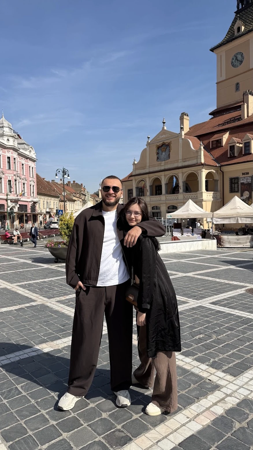 Vasile and Cleopatra Ropot, smiling, standing side by side in a sunny town square.